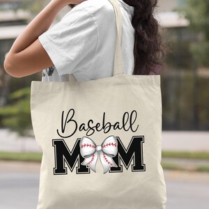 May include: A natural canvas tote bag with black text that reads "Baseball Mom" and a white and red baseball-themed bow.