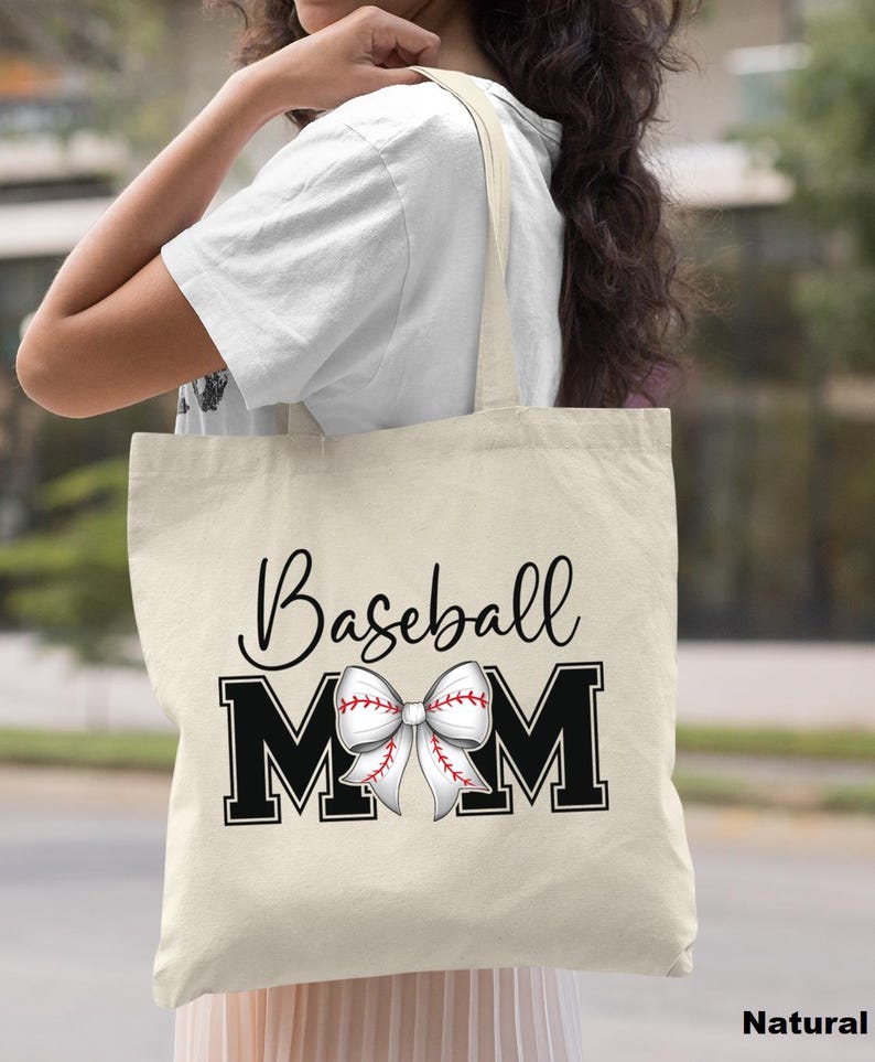 May include: A natural canvas tote bag with black text that reads "Baseball Mom" and a white and red baseball-themed bow.