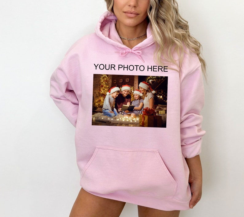 May include: Pink hoodie with a pocket and a photo of a family in Santa hats in front of a Christmas tree. The text "YOUR PHOTO HERE" is printed above the photo.