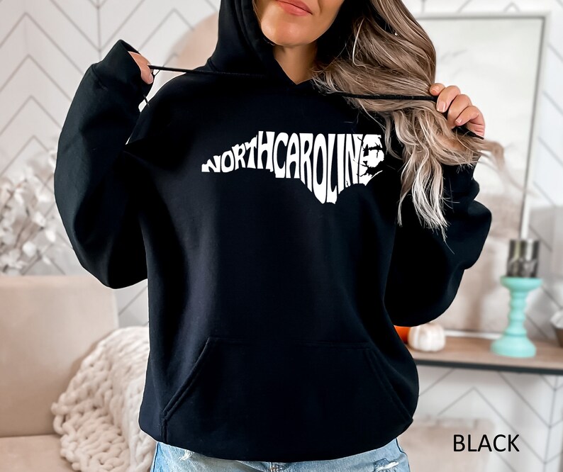 K&ouml;nnte beinhalten: Schwarzer Kapuzenpullover mit einem wei&szlig;en Umriss des Bundesstaates North Carolina und dem Text "NORTH CAROLINA" innerhalb des Umrisses.