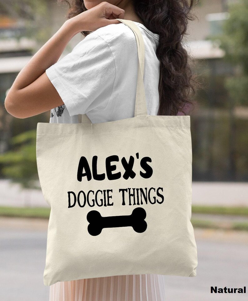 A woman carrying a white tote bag with the text "ALEX'S DOGGIE THINGS" printed on it.