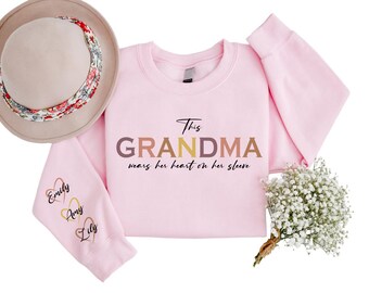 May include: Pink sweatshirt with the text "This Grandma wears her heart on her sleeve" in colorful letters. The sleeves have three hearts with the names "Emily", "Amy", and "Lily" on them.