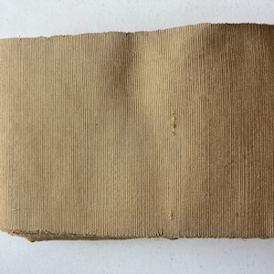 Può includere: Un rotolo di nastro in tessuto beige con una trama a coste.