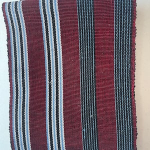 Può includere: Un pezzo di stoffa piegato con un motivo a righe in tonalità di rosso, nero, bianco e blu.
