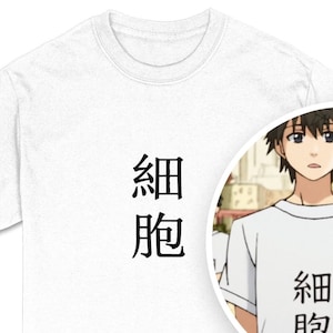 May include: White t-shirt with the Japanese characters for "cell" printed in black. The shirt is a crew neck style and appears to be made of cotton. A circular inset shows a cartoon character wearing the same shirt.