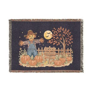 May include: A woven throw blanket featuring a dark blue background with a scarecrow in blue overalls, a yellow moon with two black bats, a tree with orange leaves, and several pumpkins. A wooden sign reads PUMPKINS, HAYRIDES, CIDER.