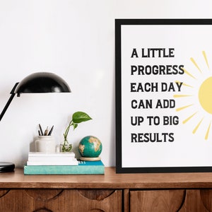 May include: A motivational quote in a black frame on a white background. The quote reads "A little progress each day can add up to big results". A yellow sun with rays is to the right of the text.
