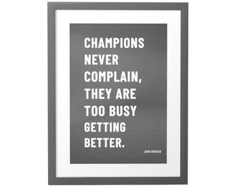 May include: A framed motivational quote in black and white. The quote reads "Champions never complain, they are too busy getting better."  The quote is attributed to John Wooden.