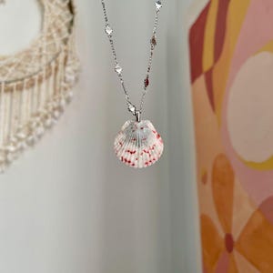 May include: A silver chain necklace with a red and white seashell pendant.