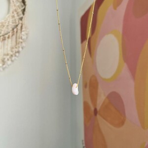 Op de afbeelding: Een delicate gouden ketting met een enkele, kleine, lichtroze schelp hanger.