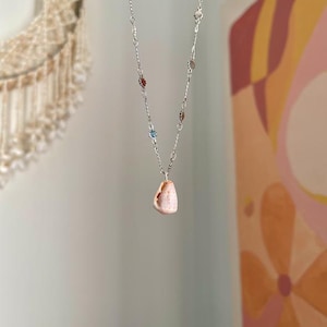 May include: A silver chain necklace with a pink shell pendant. The chain has small silver and blue beads.