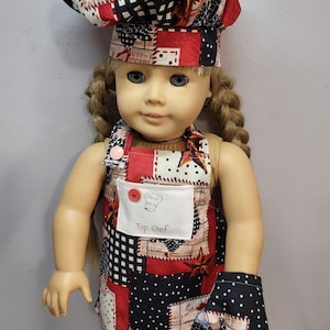 May include: A doll wearing a red and black patchwork chef's hat and matching apron with a white patch that says "Top Chef". The doll is also wearing a black and white polka dot oven mitt.
