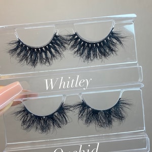 May include: Two pairs of false eyelashes in clear plastic packaging. The top pair is labeled "Whitley" and the bottom pair is labeled "Orchid".
