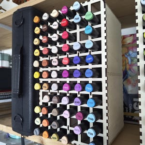 May include: A wooden marker organizer with a black carrying case on the left side. The organizer holds numerous colorful markers, each with a unique number. The markers are arranged in a grid-like pattern.