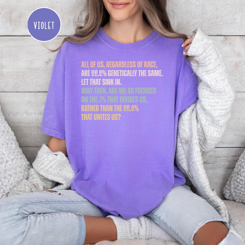 May include: A violet-colored t-shirt with the word "VIOLET" in a circle at the top left. The shirt features text in various colors: pink, green, and purple, with a message about unity and genetics.