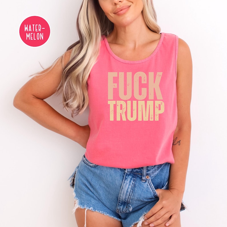 K&ouml;nnte beinhalten: Ein pinkfarbenes Tanktop mit den Worten "FUCK TRUMP" in Beige aufgedruckt. Das Tanktop wird mit Jeansshorts kombiniert. Ein "WATER-MELON"-Aufkleber befindet sich in der oberen linken Ecke.