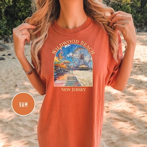May include: A rust-colored t-shirt with a graphic of a Ferris wheel and boardwalk scene. The text "Wildwood Beach New Jersey" is printed on the shirt.
