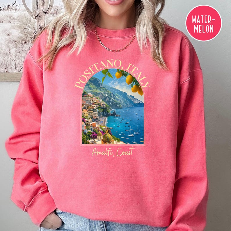 K&ouml;nnte beinhalten: Ein rosafarbenes Sweatshirt mit einem Grafikdruck von Positano, Italien. Die Grafik zeigt eine malerische Aussicht auf die Amalfik&uuml;ste mit einem Zitronenbaum und dem Text "Positano, Italien" und "Amalfik&uuml;ste".