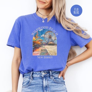 May include: A blue t-shirt with a watercolor illustration of the Wildwood Beach boardwalk in New Jersey. The illustration features a Ferris wheel, beach umbrellas, and a boardwalk.