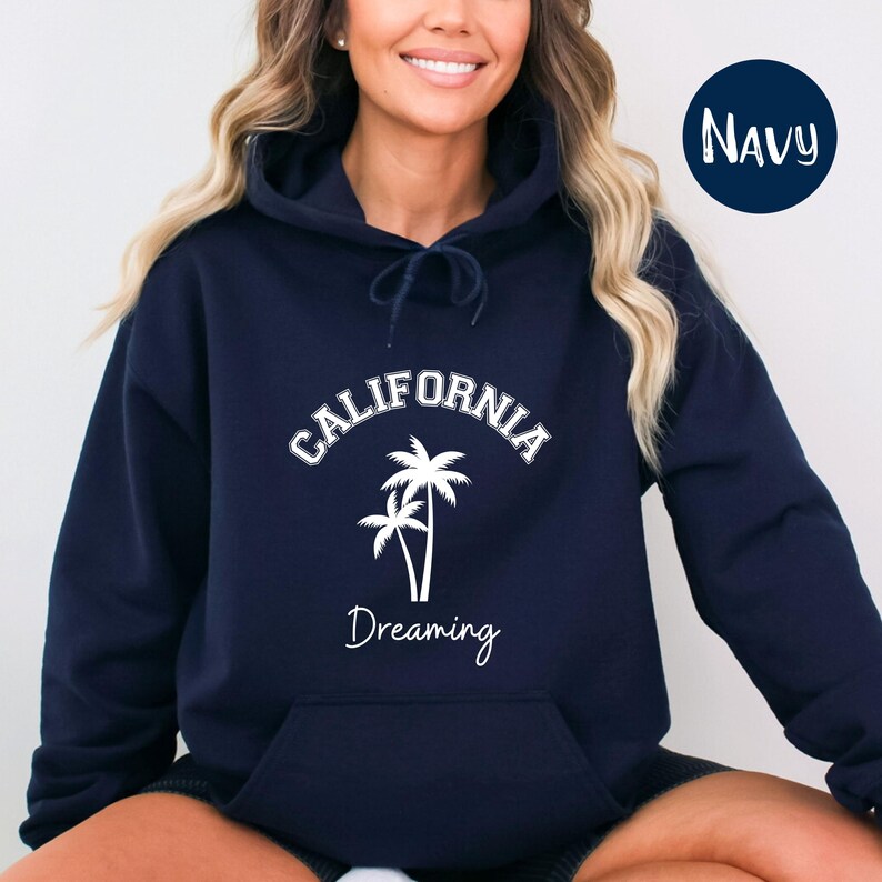 Puede incluir: Una sudadera con capucha azul marino con un gr&aacute;fico blanco de palmeras y el texto "CALIFORNIA Dreaming".