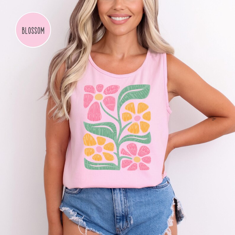 K&ouml;nnte beinhalten: Ein pinkfarbenes &auml;rmelloses Tanktop mit einem Blumendesign mit gelben, rosa und gr&uuml;nen Blumen. Der Text "BLOSSOM" befindet sich in einem pinkfarbenen Kreis oben links im Bild.