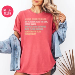 May include: A red t-shirt with the text "ALL OF US, REGARDLESS OF RACE, ARE 99.9% GENETICALLY THE SAME. LET THAT SINK IN. WHY THEN, ARE WE SO FOCUSED ON THE .1% THAT DIVIDES US, RATHER THAN THE 99.9% THAT UNITES US?"
