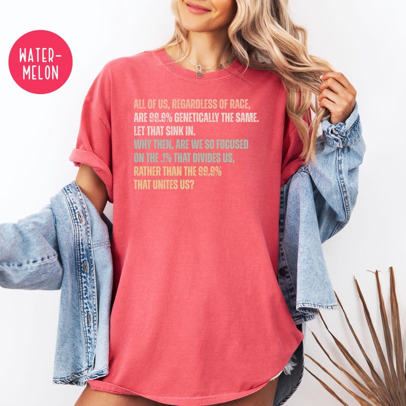 May include: A red t-shirt with the text "ALL OF US, REGARDLESS OF RACE, ARE 99.9% GENETICALLY THE SAME. LET THAT SINK IN. WHY THEN, ARE WE SO FOCUSED ON THE .1% THAT DIVIDES US, RATHER THAN THE 99.9% THAT UNITES US?"