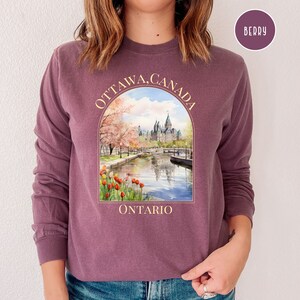 May include: A purple long-sleeved sweatshirt with a graphic print of the Parliament Building in Ottawa, Canada. The graphic includes the text "OTTAWA, CANADA" and "ONTARIO".