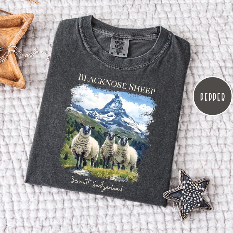 K&ouml;nnte beinhalten: Dunkelgraues T-Shirt mit einem Aufdruck von Schwarznasenschafen vor einer Berglandschaft. Der Text "BLACKNOSE SHEEP" und "Zermatt, Switzerland" ist aufgedruckt. Marke Comfort Colors.