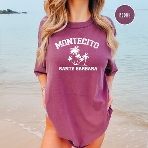 May include: A purple t-shirt with the text "Montecito Santa Barbara" and a graphic of palm trees in white.