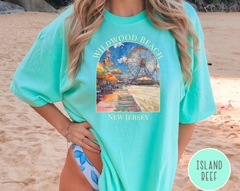May include: A turquoise blue t-shirt with a graphic print of a Ferris wheel and boardwalk scene. The text "Wildwood Beach New Jersey" is printed on the shirt.