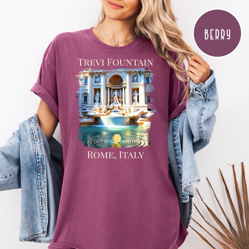 May include: Berry-coloured t-shirt with a graphic of the Trevi Fountain in Rome, Italy. The design shows the fountain's architecture, water, and a coin. The text "TREVI FOUNTAIN" and "ROME, ITALY" are printed on the shirt.