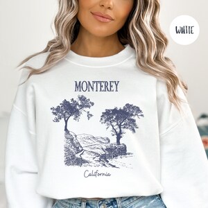 May include: White sweatshirt with a blue graphic print of trees and a road leading to the text "Monterey, California".