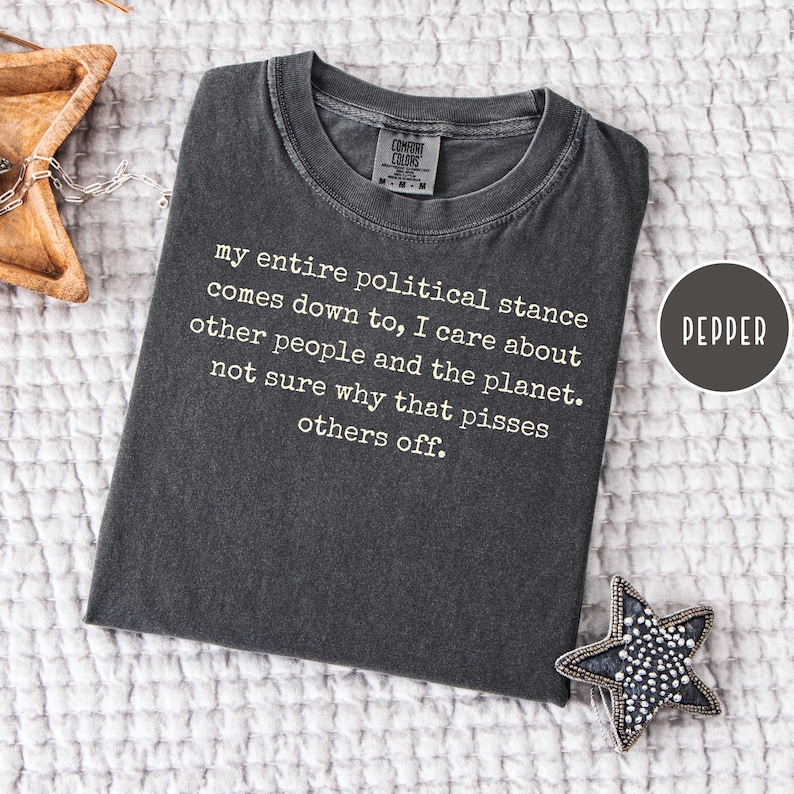 May include: A dark grey t-shirt with the text "my entire political stance comes down to, I care about other people and the planet. not sure why that pisses others off." A round label reads "PEPPER".