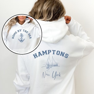 May include: White hooded sweatshirt with a blue anchor and the text "Home by the Sea" on the front and the text "HAMPTONS New York" with a sailboat graphic on the back.
