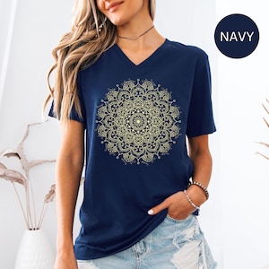 May include: A navy blue v-neck t-shirt with a gold mandala design. The mandala is intricate and detailed, with a circular pattern of flowers and leaves.