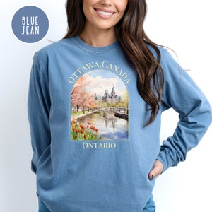 May include: A blue jean long-sleeve sweatshirt with a graphic print of the Parliament Building in Ottawa, Canada. The graphic includes the text "Ottawa, Canada" and "Ontario".