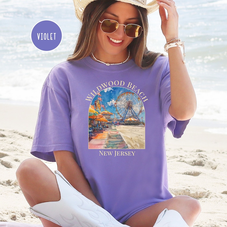 May include: A purple t-shirt with a graphic of a Ferris wheel and boardwalk scene. The text "Wildwood Beach New Jersey" is printed on the shirt.