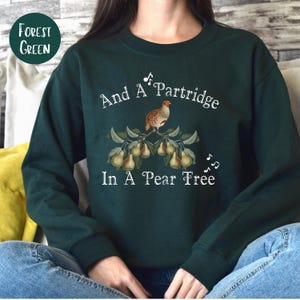 May include: A dark green sweatshirt with the text "And A Partridge In A Pear Tree" printed in white. The design features a partridge perched on a branch with pears.