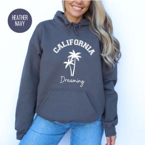 Puede incluir: Sudadera con capucha de color azul marino jaspeado con el texto "CALIFORNIA DREAMING" en letras blancas y un gr&aacute;fico de dos palmeras.