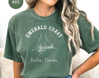 May include: A moss green t-shirt with a white graphic of a sailboat and the text "EMERALD COAST Destin, Florida".