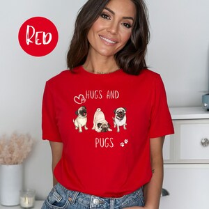 Puede incluir: Una camiseta roja con un gr&aacute;fico blanco de tres carlinos y el texto "Hugs and Pugs".