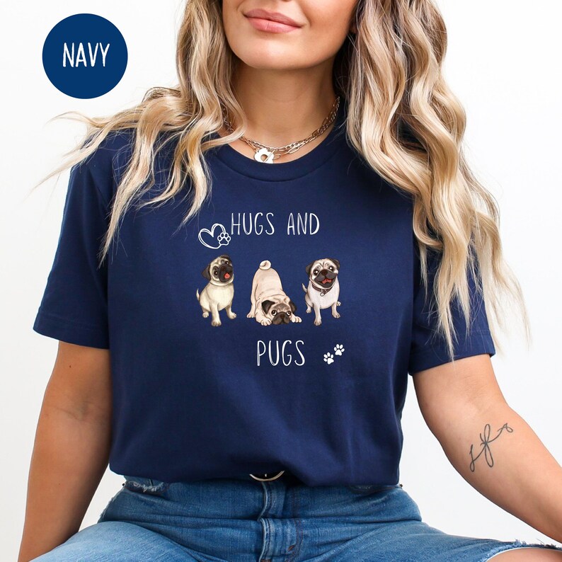 Puede incluir: Una camiseta azul marino con un gr&aacute;fico blanco de tres carlinos y el texto "Hugs and Pugs".