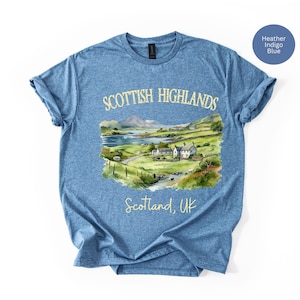 Puede incluir: Camiseta azul &iacute;ndigo jaspeado con una ilustraci&oacute;n en acuarela de las Tierras Altas escocesas. El dise&ntilde;o incluye un paisaje con monta&ntilde;as, un lago y edificios. El texto en la camiseta dice "Scottish Highlands" y "Scotland, UK."
