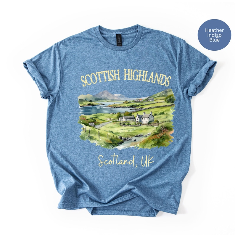 Puede incluir: Camiseta azul &iacute;ndigo jaspeado con una ilustraci&oacute;n en acuarela de las Tierras Altas escocesas. El dise&ntilde;o incluye un paisaje con monta&ntilde;as, un lago y edificios. El texto en la camiseta dice "Scottish Highlands" y "Scotland, UK."