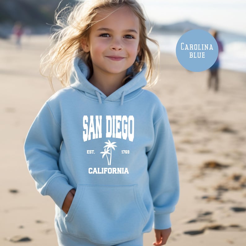 May include: A light blue hoodie with the text "SAN DIEGO" in white block letters, along with "EST. 1769" and "CALIFORNIA" and a palm tree graphic. The hoodie has a front pocket and a hood.