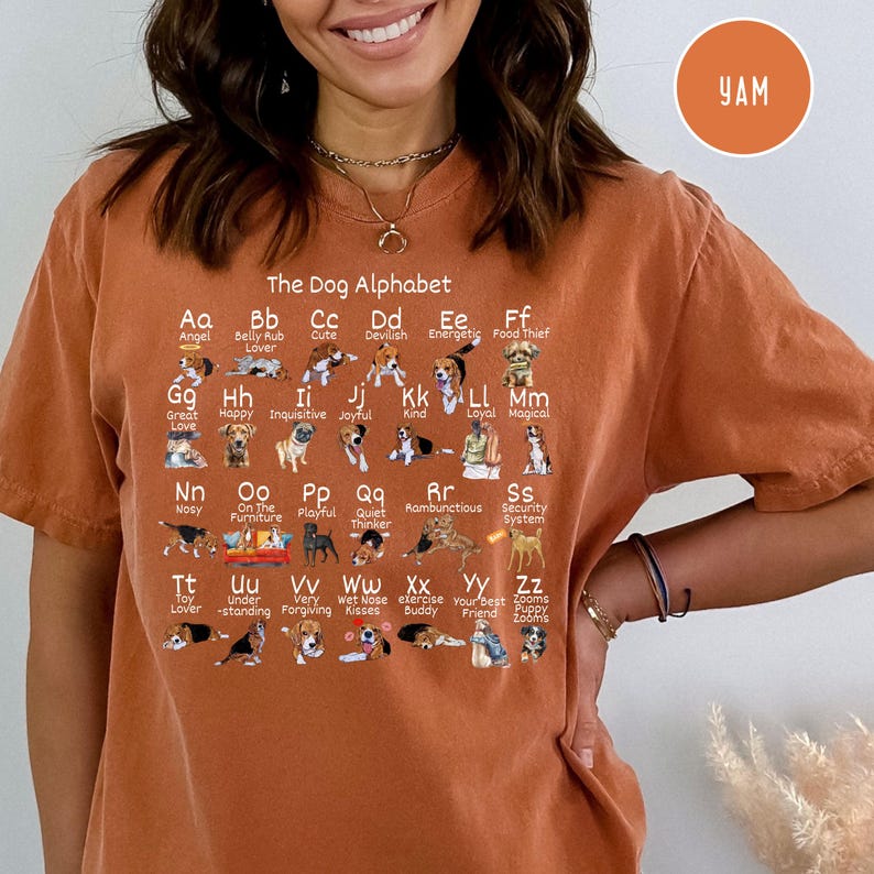 May include: A brown t-shirt with a graphic of a dog alphabet. Each letter of the alphabet is represented by a dog breed with a corresponding word describing the breed. The text "The Dog Alphabet" is at the top of the graphic.