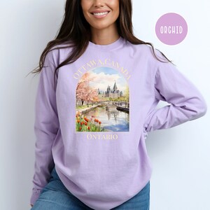 May include: A lavender long-sleeve sweatshirt with a graphic print of the Parliament Building in Ottawa, Canada. The graphic includes the text "OTTAWA, CANADA" and "ONTARIO".