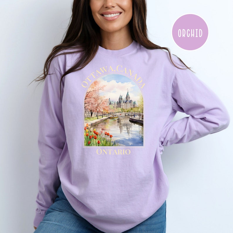 May include: A lavender long-sleeve sweatshirt with a graphic print of the Parliament Building in Ottawa, Canada. The graphic includes the text "OTTAWA, CANADA" and "ONTARIO".