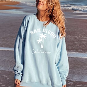 May include: A light blue sweatshirt with a white graphic print of palm trees and the text "SAN DIEGO California".